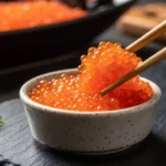 Bright orange tobiko (flying fish roe) in a ceramic dish.